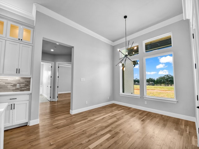 unfurnished dining area with crown molding, a notable chandelier, and hardwood / wood-style flooring