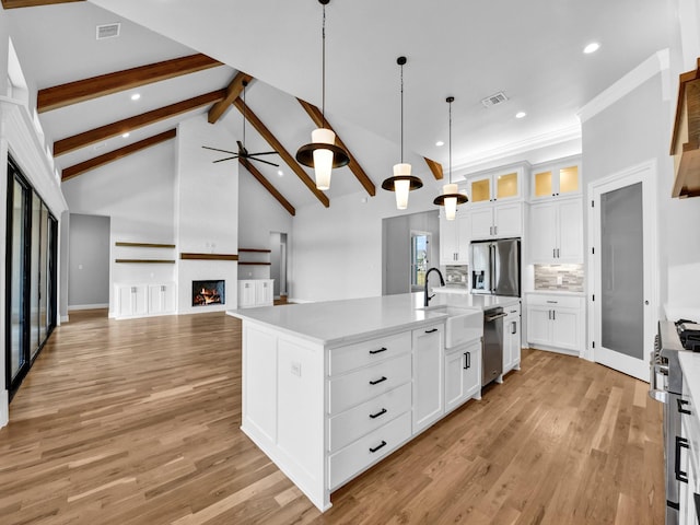 kitchen featuring a fireplace, an island with sink, white cabinets, hanging light fixtures, and stainless steel appliances