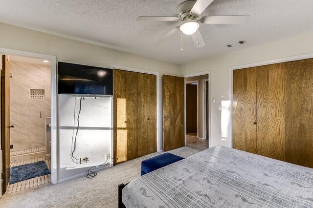 unfurnished bedroom featuring ensuite bath, light carpet, a textured ceiling, two closets, and ceiling fan