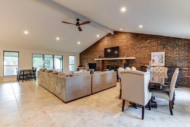 living room featuring lofted ceiling with beams, ceiling fan, brick wall, and a fireplace