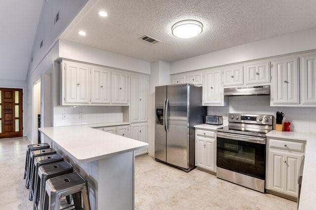 kitchen with appliances with stainless steel finishes, a breakfast bar area, white cabinets, backsplash, and kitchen peninsula