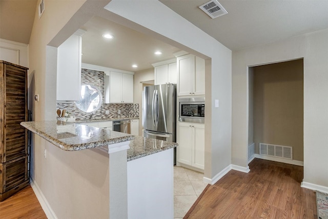 kitchen with white cabinetry, appliances with stainless steel finishes, kitchen peninsula, light stone countertops, and backsplash