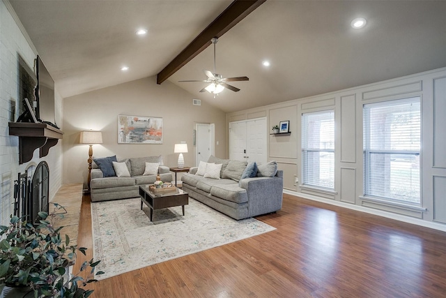 living room featuring hardwood / wood-style flooring, ceiling fan, a fireplace, and vaulted ceiling with beams