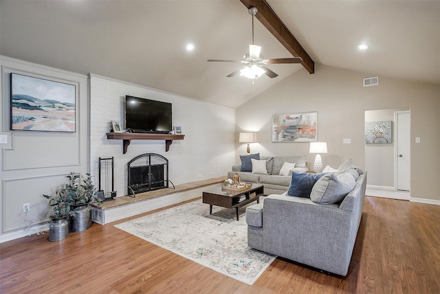 living room featuring ceiling fan, hardwood / wood-style floors, a brick fireplace, and vaulted ceiling with beams