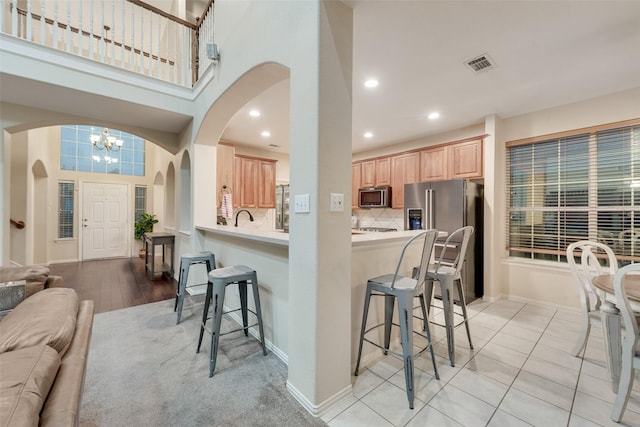 kitchen with tasteful backsplash, a kitchen bar, a notable chandelier, kitchen peninsula, and stainless steel appliances