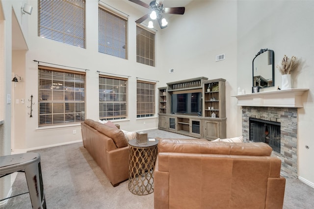 living room with ceiling fan, a stone fireplace, carpet, and a towering ceiling