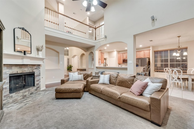 living room featuring light carpet, ceiling fan with notable chandelier, and a fireplace