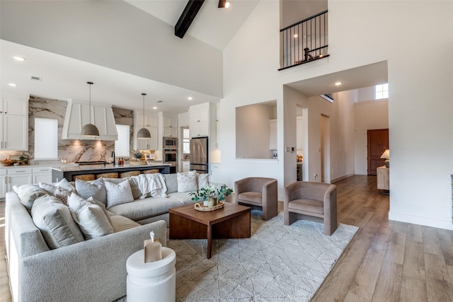 living room featuring beamed ceiling, a towering ceiling, and light wood-type flooring