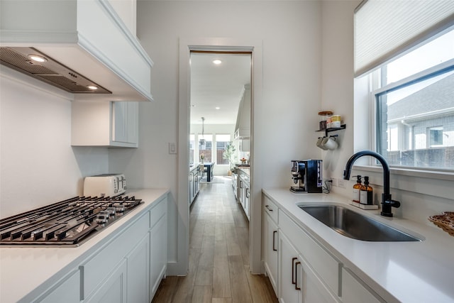 kitchen featuring stainless steel gas stovetop, white cabinetry, sink, and custom exhaust hood