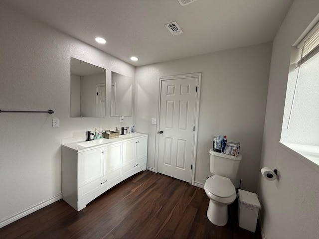 full bath with double vanity, baseboards, visible vents, toilet, and wood finished floors