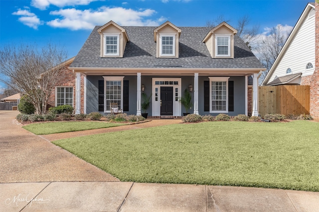 new england style home featuring roof with shingles, brick siding, a front lawn, and a porch