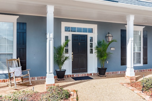 property entrance featuring a porch, a shingled roof, and stucco siding