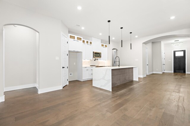 kitchen featuring dark hardwood / wood-style flooring, hanging light fixtures, white cabinets, and a center island with sink
