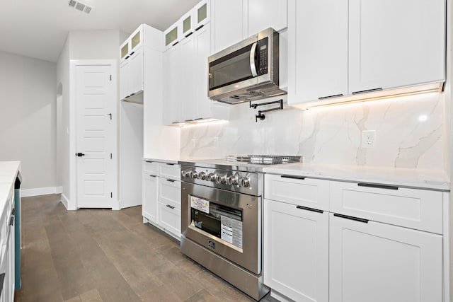 kitchen featuring appliances with stainless steel finishes, white cabinetry, hardwood / wood-style floors, light stone counters, and tasteful backsplash