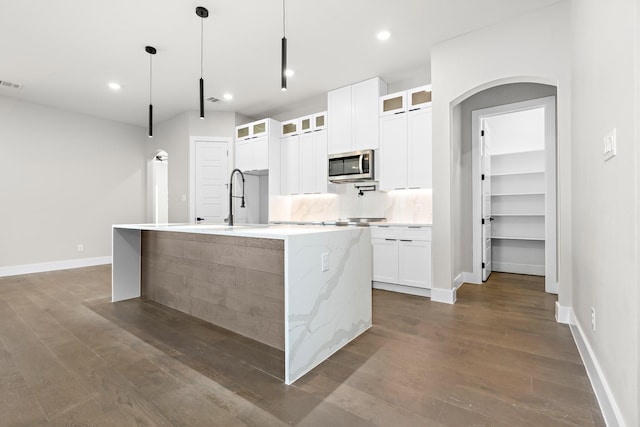 kitchen with white cabinetry, a kitchen island with sink, pendant lighting, and dark wood-type flooring