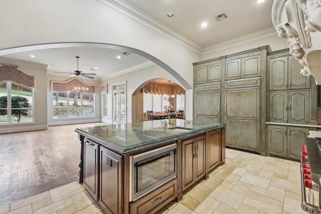 kitchen featuring stainless steel microwave, sink, ceiling fan, crown molding, and a center island with sink