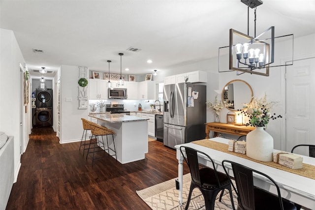 kitchen with decorative light fixtures, sink, white cabinets, stacked washer and clothes dryer, and stainless steel appliances