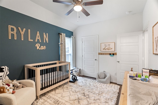 bedroom featuring a crib, wood-type flooring, lofted ceiling, and ceiling fan