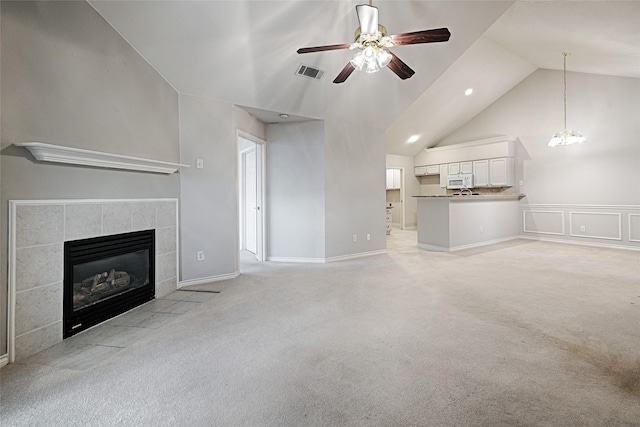 unfurnished living room with light colored carpet, high vaulted ceiling, a tiled fireplace, and ceiling fan with notable chandelier