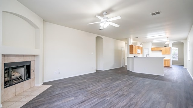 unfurnished living room featuring ceiling fan, wood-type flooring, and a tile fireplace