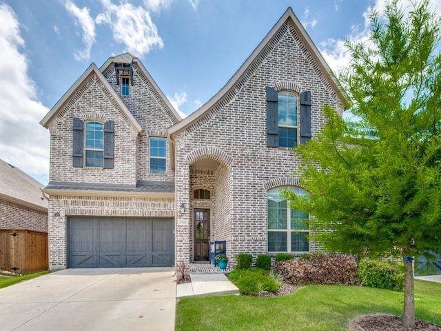 french country style house with a garage, concrete driveway, fence, a front lawn, and brick siding