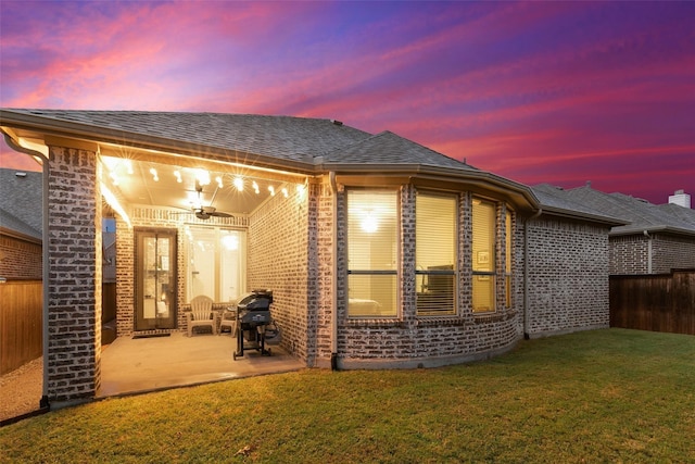 back house at dusk with ceiling fan, a yard, and a patio area