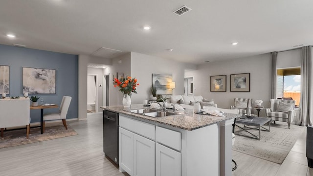 kitchen with sink, dishwasher, light stone counters, an island with sink, and white cabinets