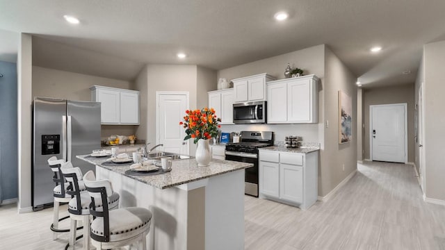 kitchen featuring sink, appliances with stainless steel finishes, light stone countertops, an island with sink, and white cabinets