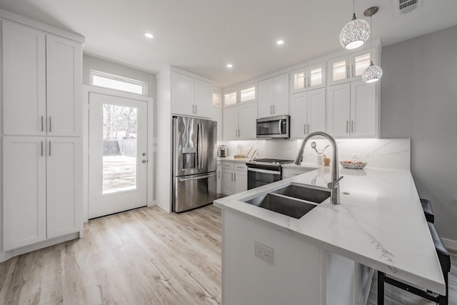 kitchen featuring white cabinetry, decorative light fixtures, kitchen peninsula, stainless steel appliances, and light hardwood / wood-style floors