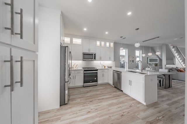 kitchen with hanging light fixtures, light wood-type flooring, kitchen peninsula, stainless steel appliances, and white cabinets