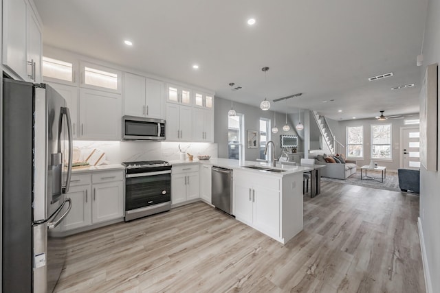 kitchen featuring sink, decorative light fixtures, kitchen peninsula, stainless steel appliances, and white cabinets