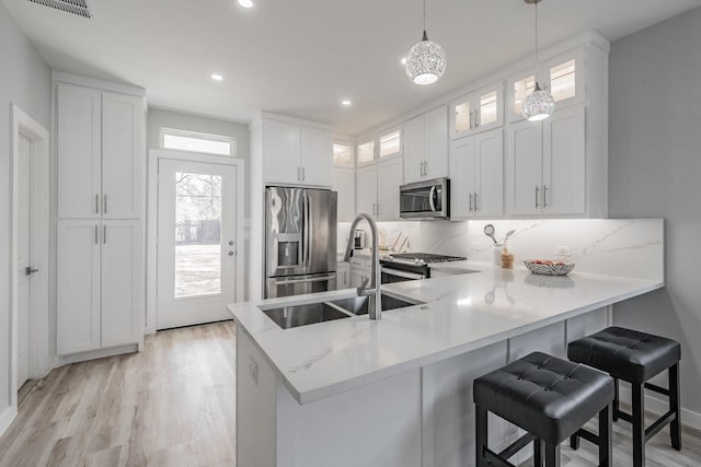 kitchen featuring decorative light fixtures, stainless steel appliances, kitchen peninsula, and white cabinets