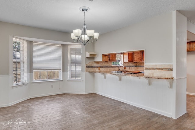 kitchen featuring an inviting chandelier, a breakfast bar area, hanging light fixtures, kitchen peninsula, and light wood-type flooring