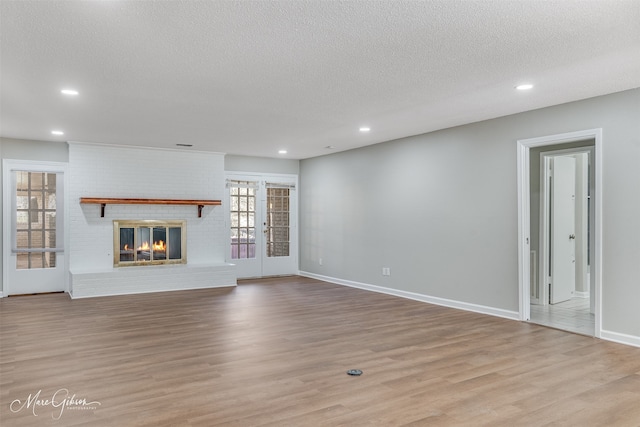 unfurnished living room featuring a textured ceiling, a fireplace, light wood-type flooring, and french doors