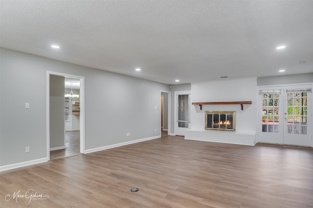 unfurnished living room featuring a textured ceiling, a fireplace, light wood-type flooring, and french doors
