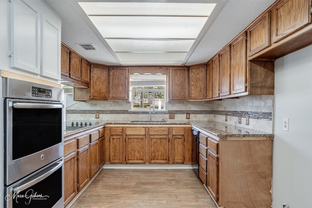 kitchen with black appliances, sink, backsplash, light stone counters, and light hardwood / wood-style floors