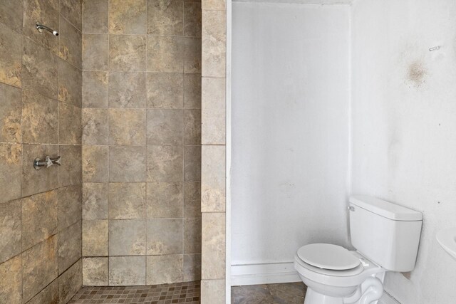 full bathroom featuring toilet, baseboards, and a tile shower
