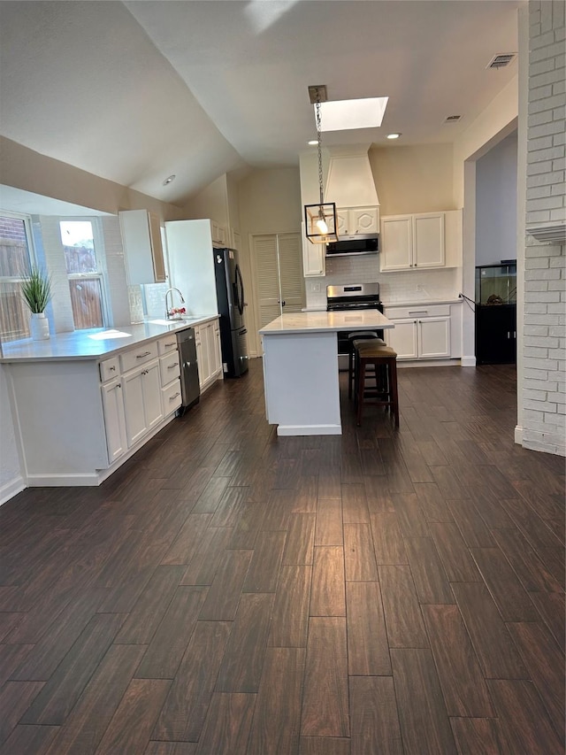 kitchen with white cabinetry, appliances with stainless steel finishes, exhaust hood, and decorative light fixtures