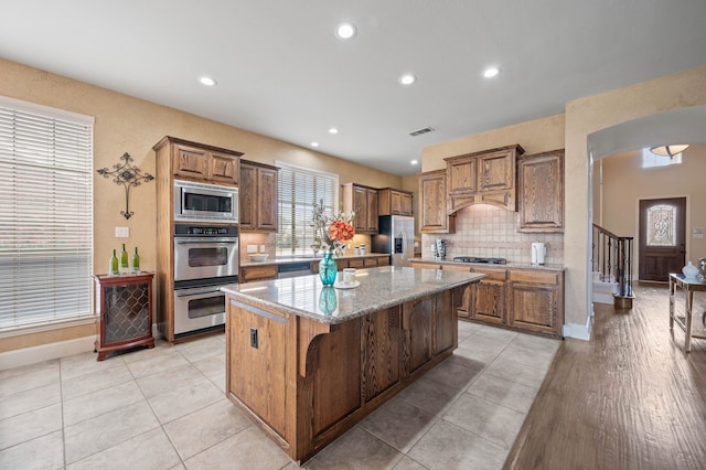 kitchen with backsplash, a kitchen island, stainless steel appliances, light stone counters, and a kitchen bar