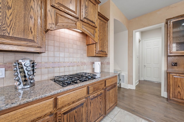 kitchen featuring light stone counters, gas cooktop, light tile patterned floors, and backsplash