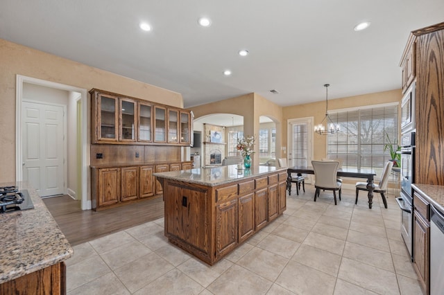 kitchen with light tile patterned floors, a notable chandelier, a kitchen island, decorative light fixtures, and oven