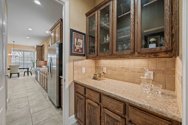 kitchen featuring stainless steel fridge, an inviting chandelier, hanging light fixtures, light stone counters, and decorative backsplash