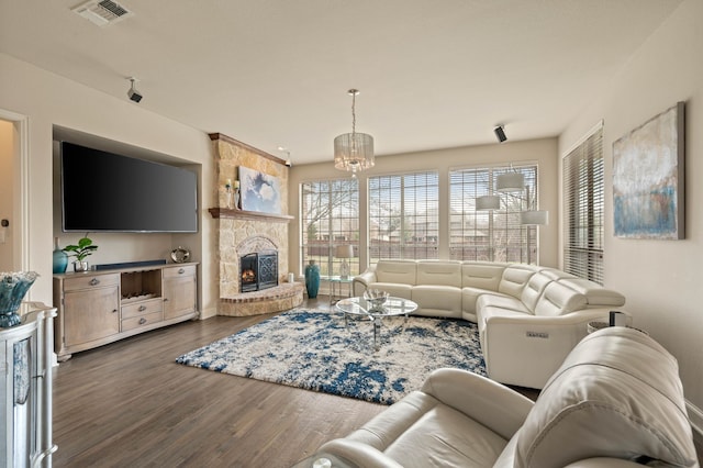 living room with dark wood-type flooring, a stone fireplace, and a notable chandelier