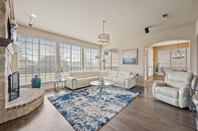 living room featuring wood-type flooring, a stone fireplace, a chandelier, and plenty of natural light