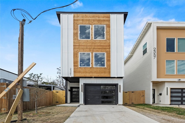 modern home featuring an attached garage, fence, board and batten siding, and concrete driveway