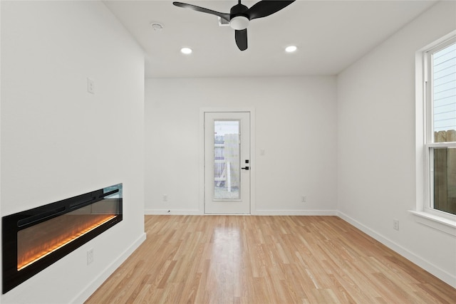 interior space featuring recessed lighting, a ceiling fan, a glass covered fireplace, light wood-type flooring, and baseboards