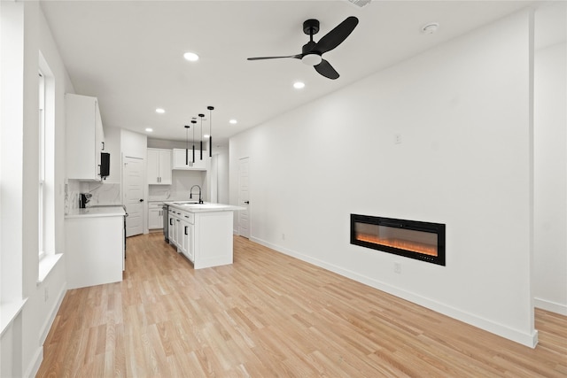 kitchen with light wood-type flooring, a glass covered fireplace, a kitchen island with sink, and a sink