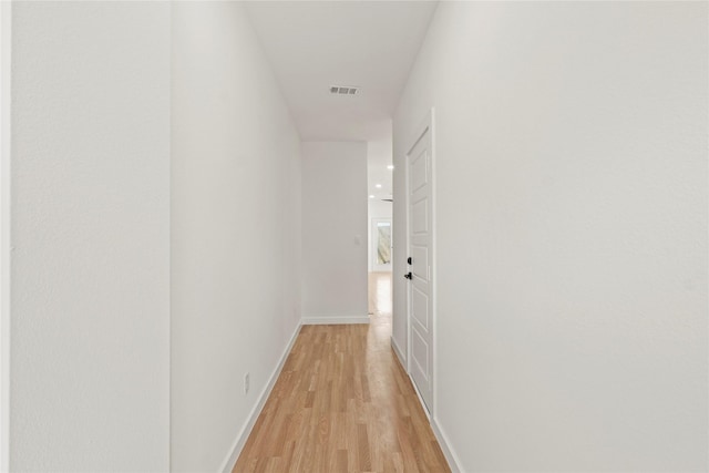 hall with light wood-style flooring, visible vents, and baseboards