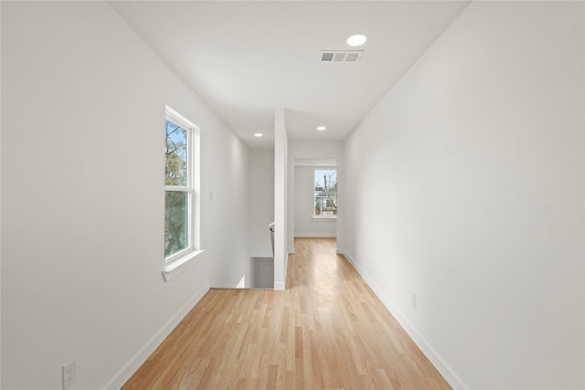 hall with baseboards, light wood-style floors, visible vents, and a healthy amount of sunlight