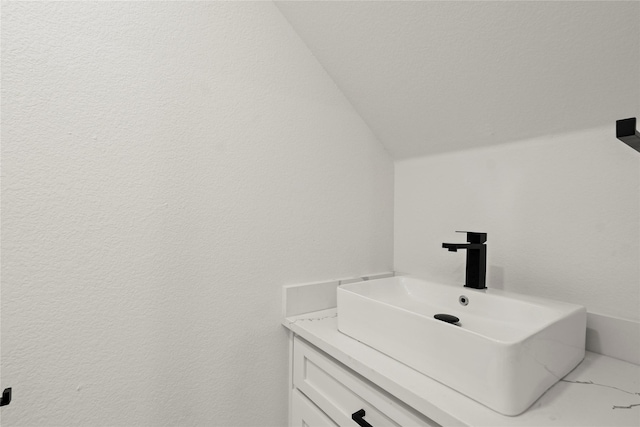 bathroom featuring a textured wall, vaulted ceiling, and vanity